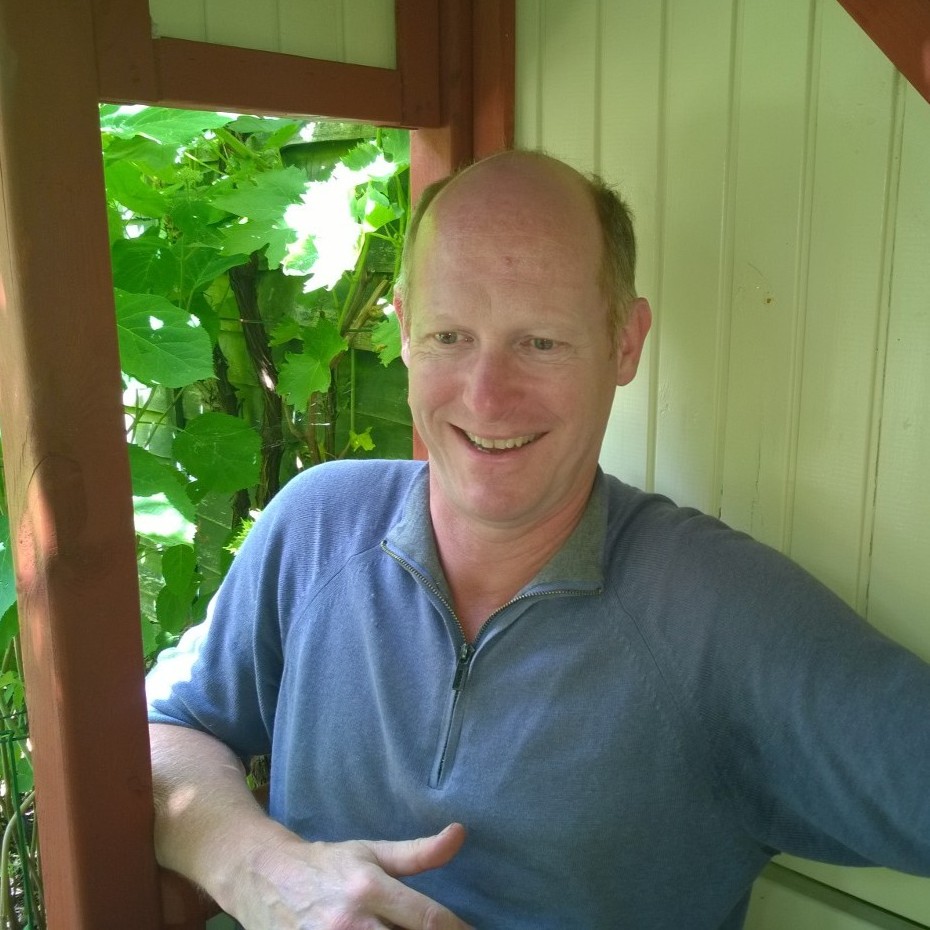 Photo of Hans Maatman, sitting in a red-and-white, wooden arbour in a garden.
